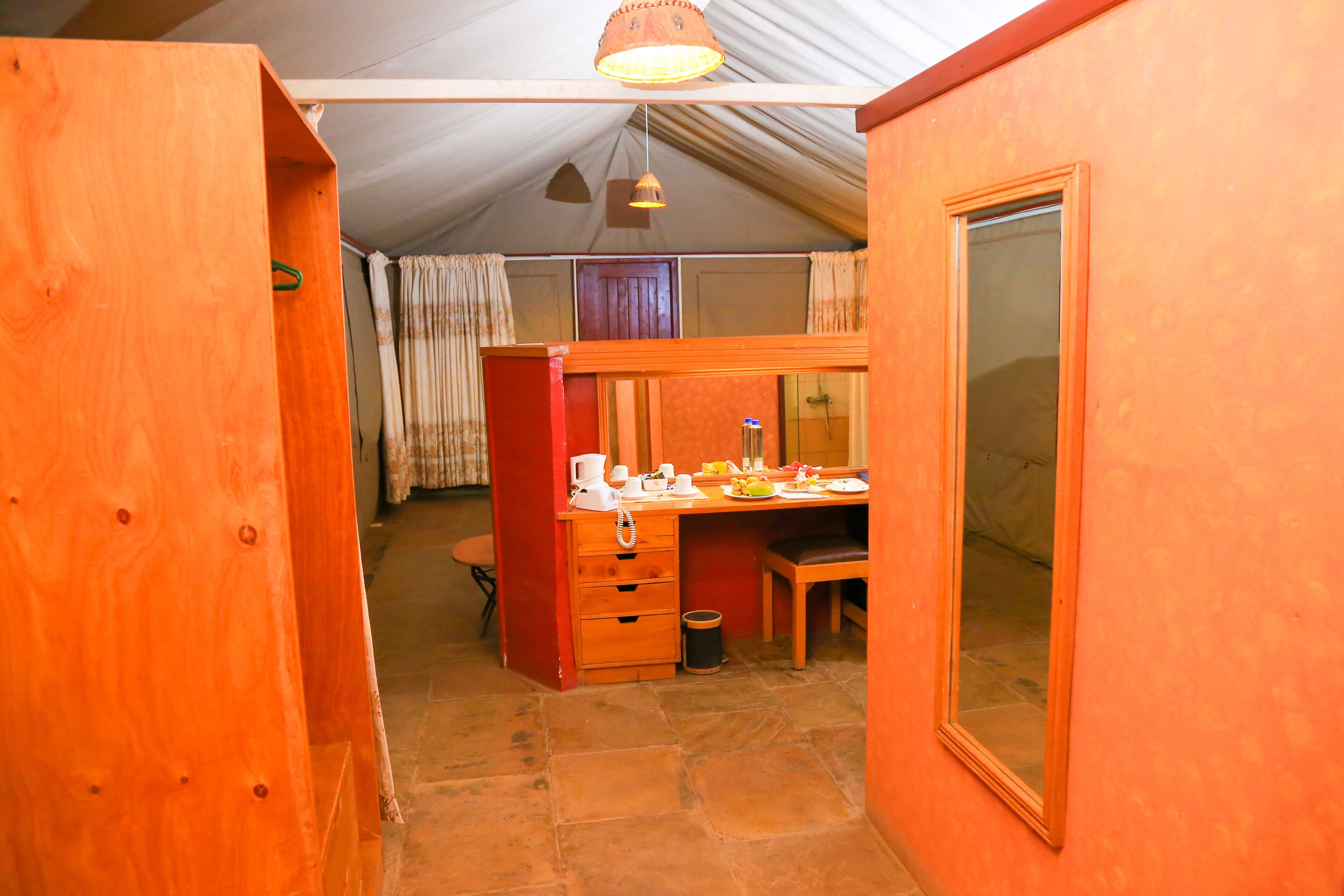 A compact room with a wooden desk, a chair, a small trash bin, and a mirror on the wall.