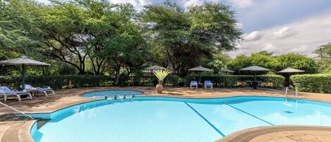 A swimming pool with tiled edges, surrounded by lounge chairs and umbrellas, set in a landscaped area with trees.
