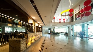 Een ruime lobby met een marmeren receptiebalie, moderne verlichtingsarmaturen en een hoge plafond met hangende decoraties.