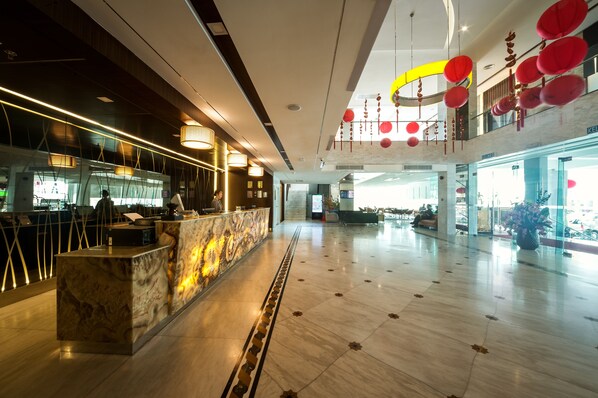 A spacious lobby with a marble reception desk, modern lighting fixtures, and a high ceiling with hanging decorations.