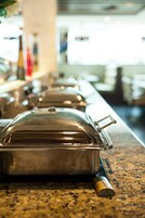 Una barra de buffet con recipientes cubiertos sobre una encimera de granito.