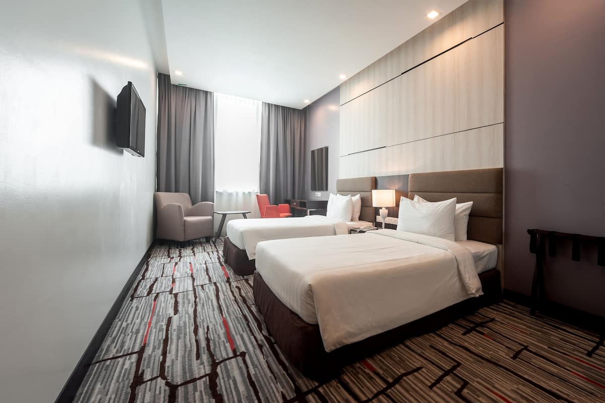 Une chambre d’hôtel avec deux lits, un bureau, une chaise, une télévision et une grande fenêtre avec des rideaux.