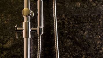 A showerhead with a control knob and a flexible hose against a dark, textured wall.