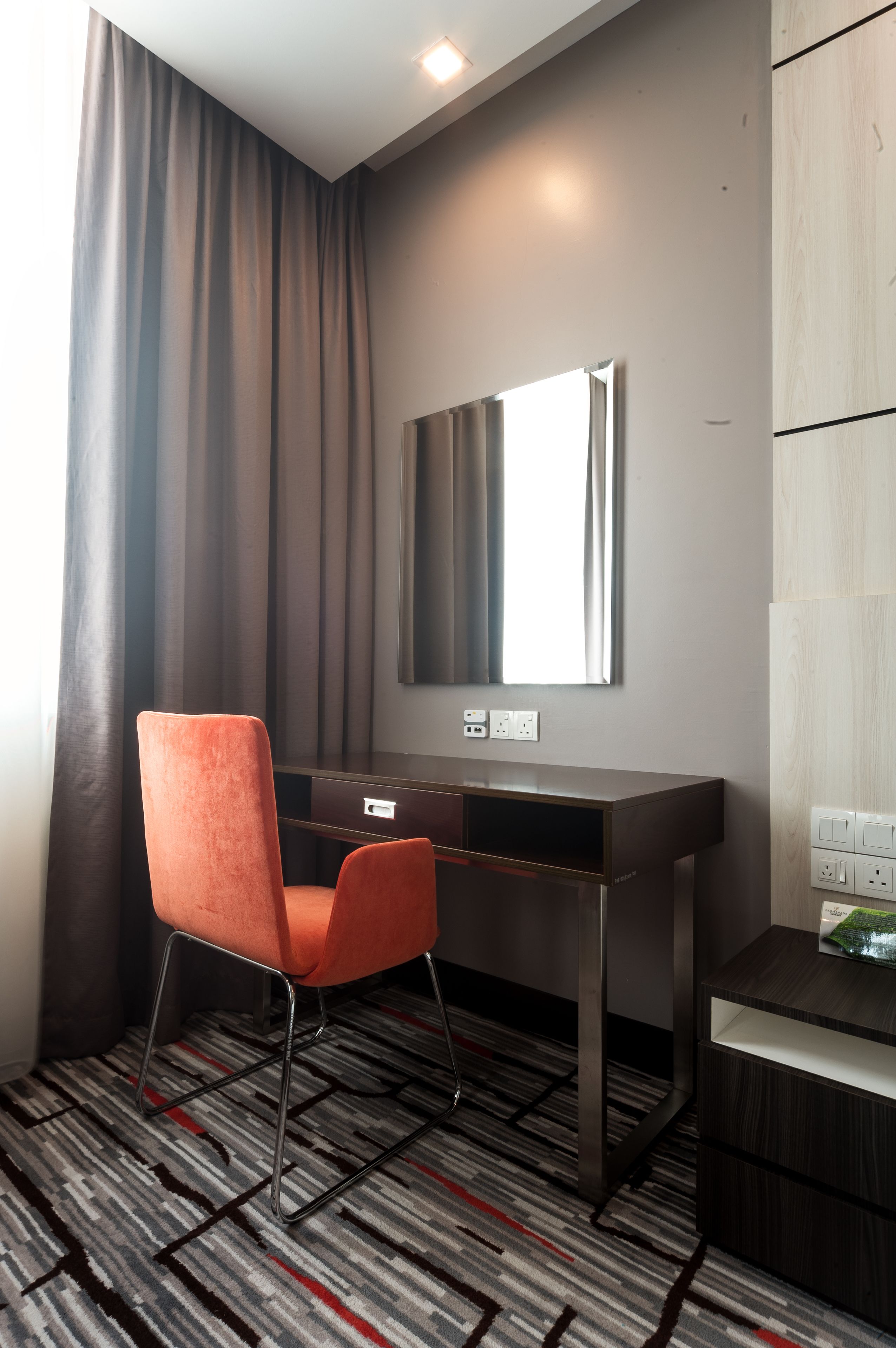 Una habitación de hotel moderna con escritorio, una silla, un espejo y una alfombra estampada.