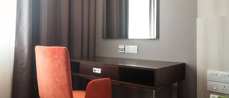 Una habitación de hotel moderna con escritorio, una silla, un espejo y una alfombra estampada.