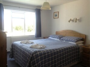 A bedroom with a wooden headboard, a checkered bedspread, two pillows, a bedside table, a lamp, a window with curtains, and a framed picture on the wall. - Blue Horizon Hotel (St. Martins)
