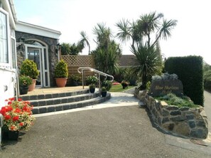 A hotel entrance with a stone pathway leading to the door, surrounded by potted plants and palm trees.
