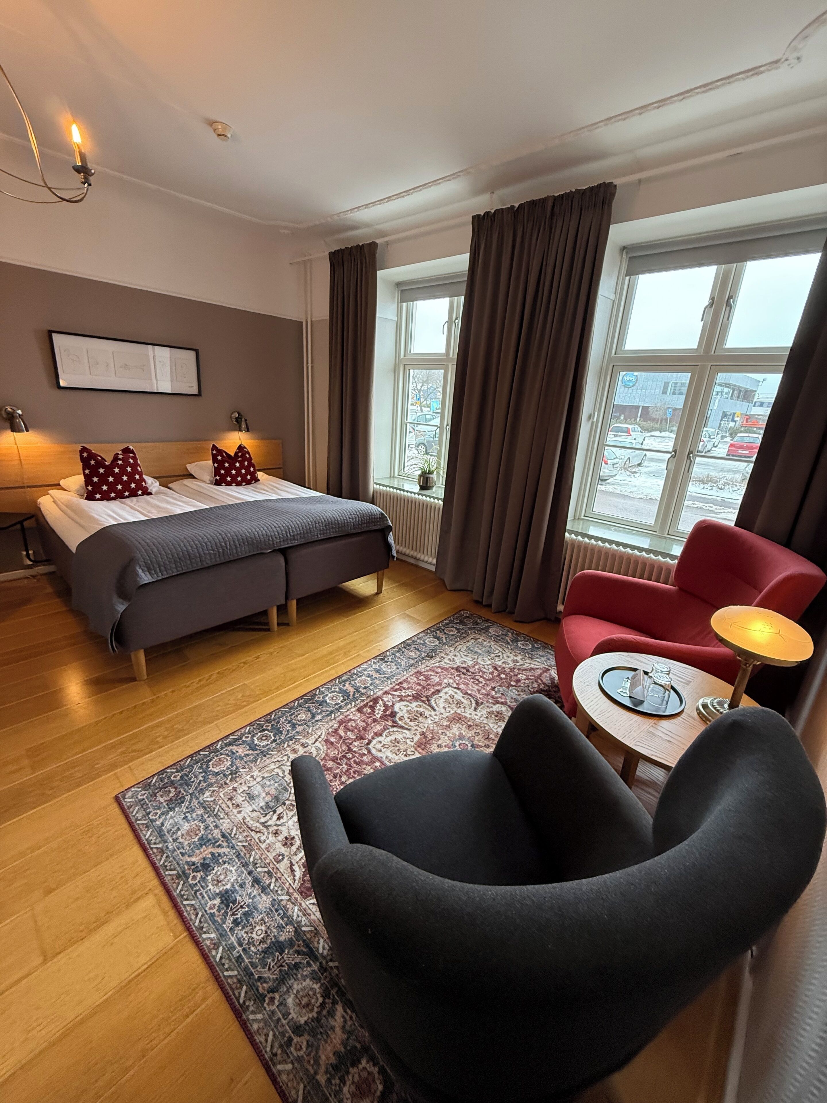 Habitación de hotel con cama, escritorio, silla, ventana con cortinas y vistas al exterior.
