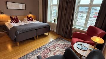 Habitación de hotel con cama, escritorio, silla, ventana con cortinas y vistas al exterior.