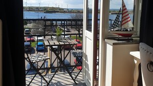 Ein Balkon mit Blick auf eine Marina, ein Modellsegelschiff und abgestellte Autos.
