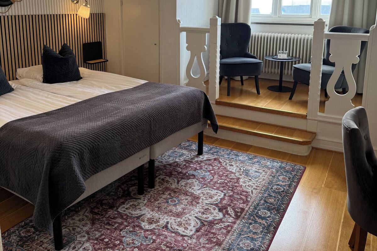 A bedroom with a bed, a bedside table, a chair, a window with curtains, and a view of the outdoors.