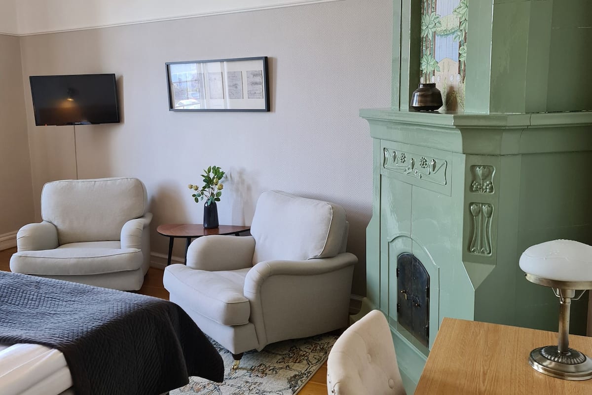 A room with a fireplace, two armchairs, a small table with a vase, and a television mounted on the wall.