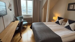 Ein Hotelzimmer mit Bett, Schreibtisch, Stuhl, Fernseher und einem Fenster mit Vorhängen.