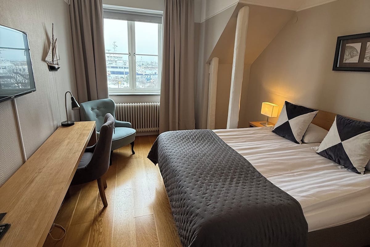 A hotel room with a bed, a desk, a chair, a TV, and a window with curtains.