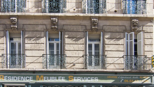 Un edificio con varios balcones, una zona de recepción y un cartel que indica que es una residencia con servicios.