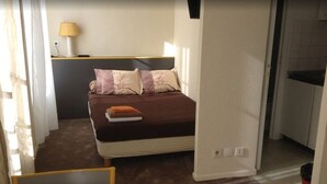 Una habitación de hotel compacta con una cama, una mesita de noche, una lámpara y una pequeña mesa.