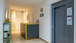 Un pasillo con mostrador de recepción, escalera y puerta con un cartel.