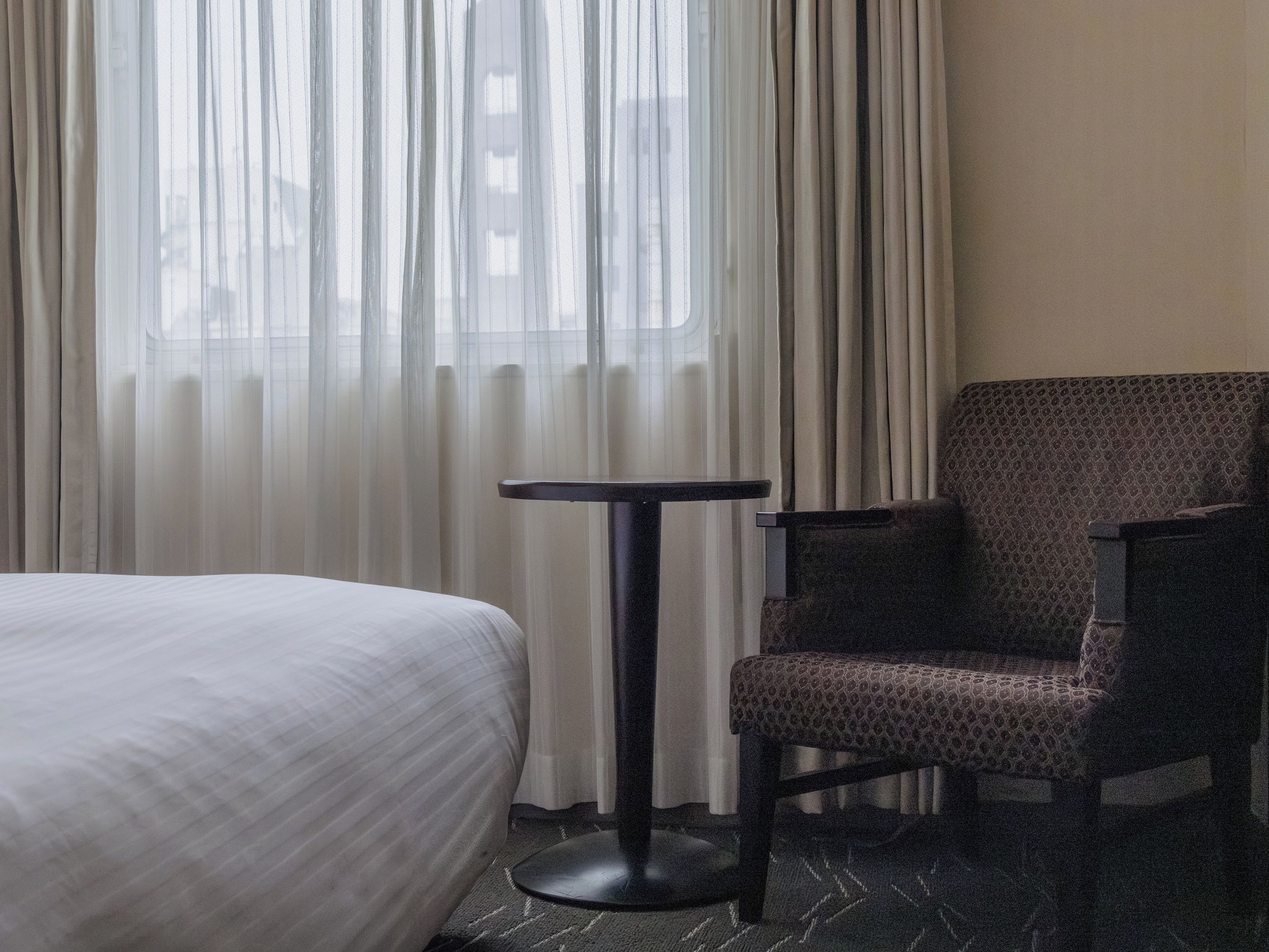 A hotel room with a bed, a chair, and a small table.