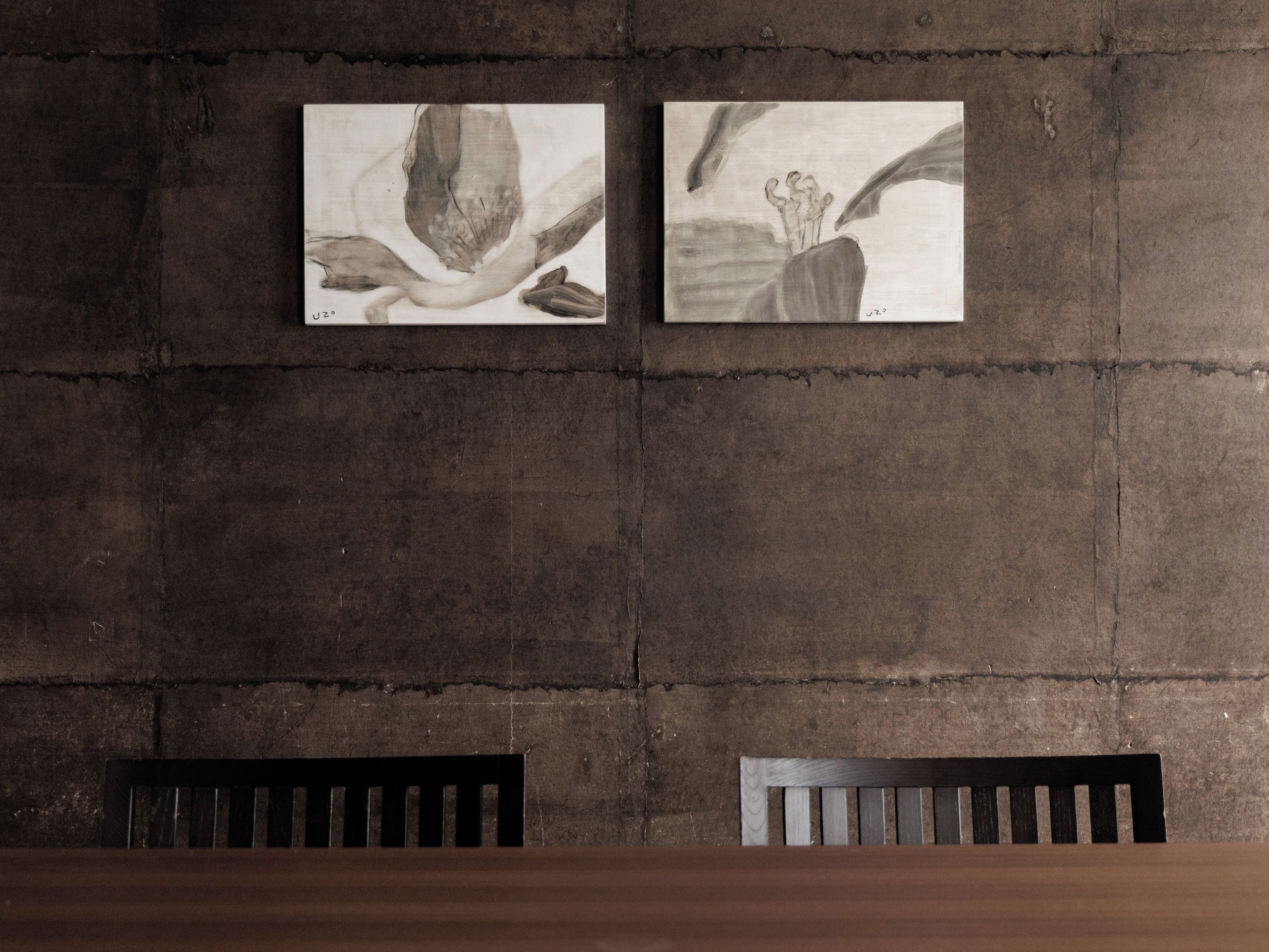 A wall with two framed artworks and two wooden chairs in front of a table.