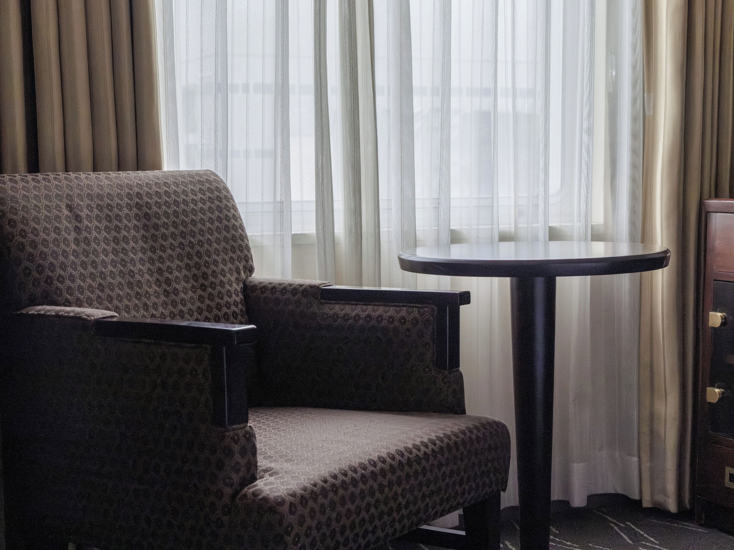 A room with a patterned armchair, a small round table, and a cabinet.