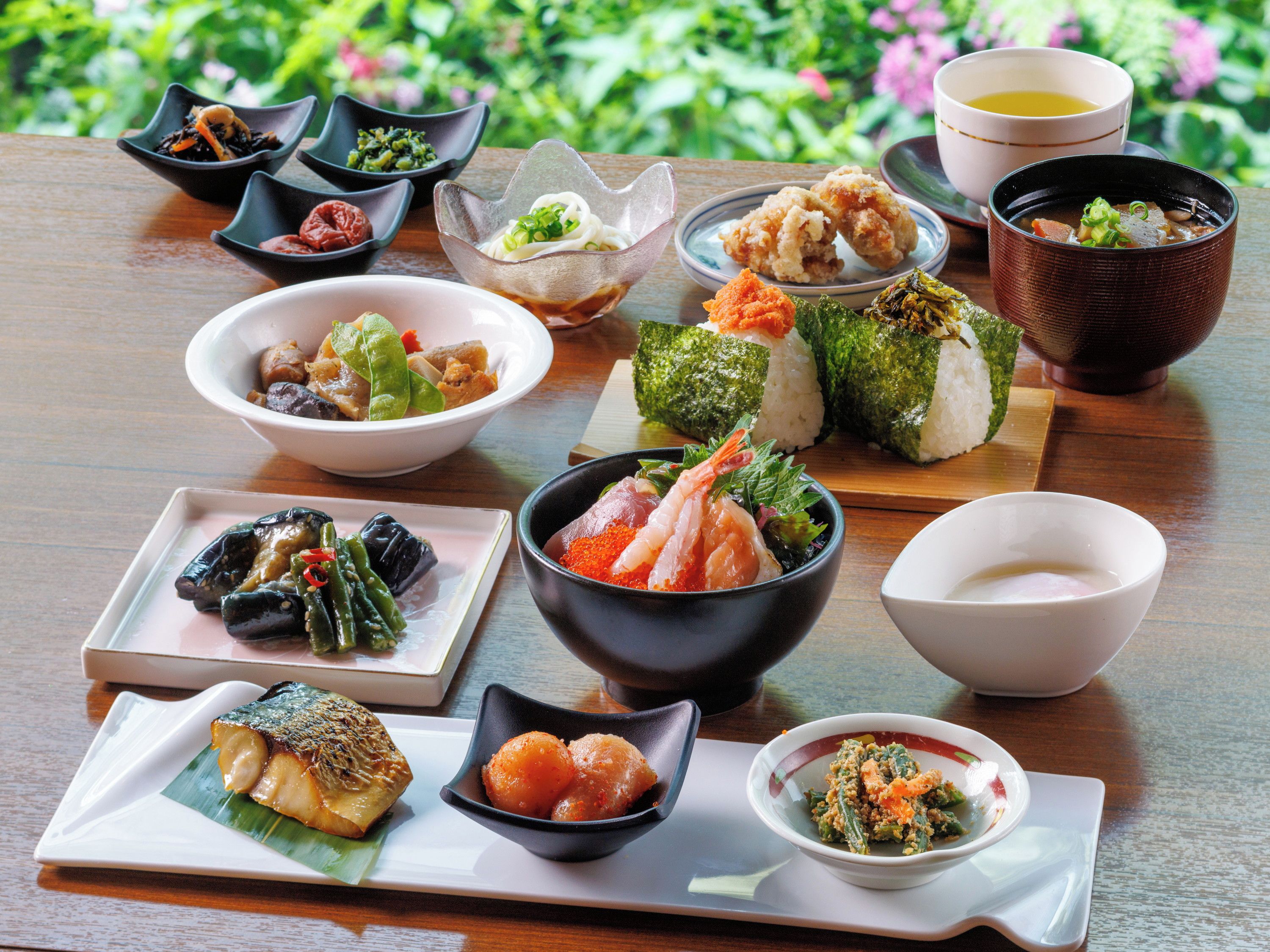 A variety of Japanese dishes arranged on a wooden table with a garden view in the background.