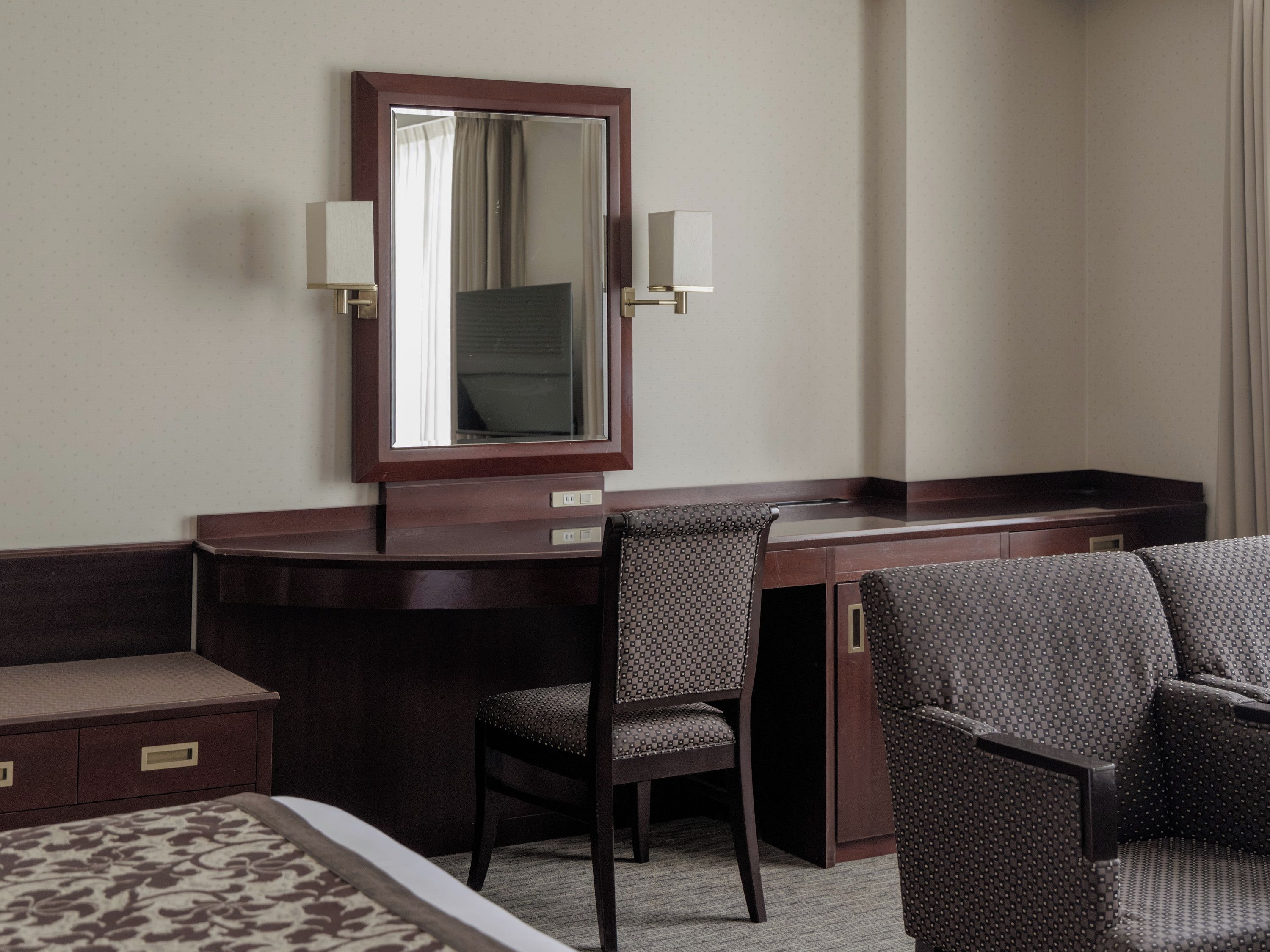 A hotel room with a desk, two chairs, a bed, and a large mirror.