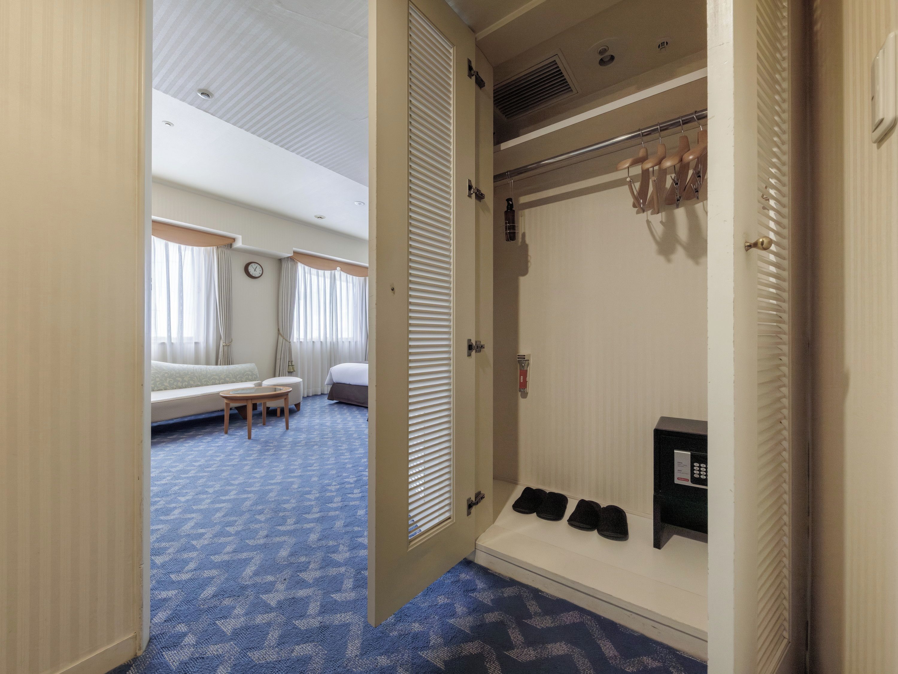 Ein Hotelzimmer mit einem Bett, einer Sitzecke mit Tisch, einem Schuhregal und einem Badezimmer mit Dusche und Toilette.