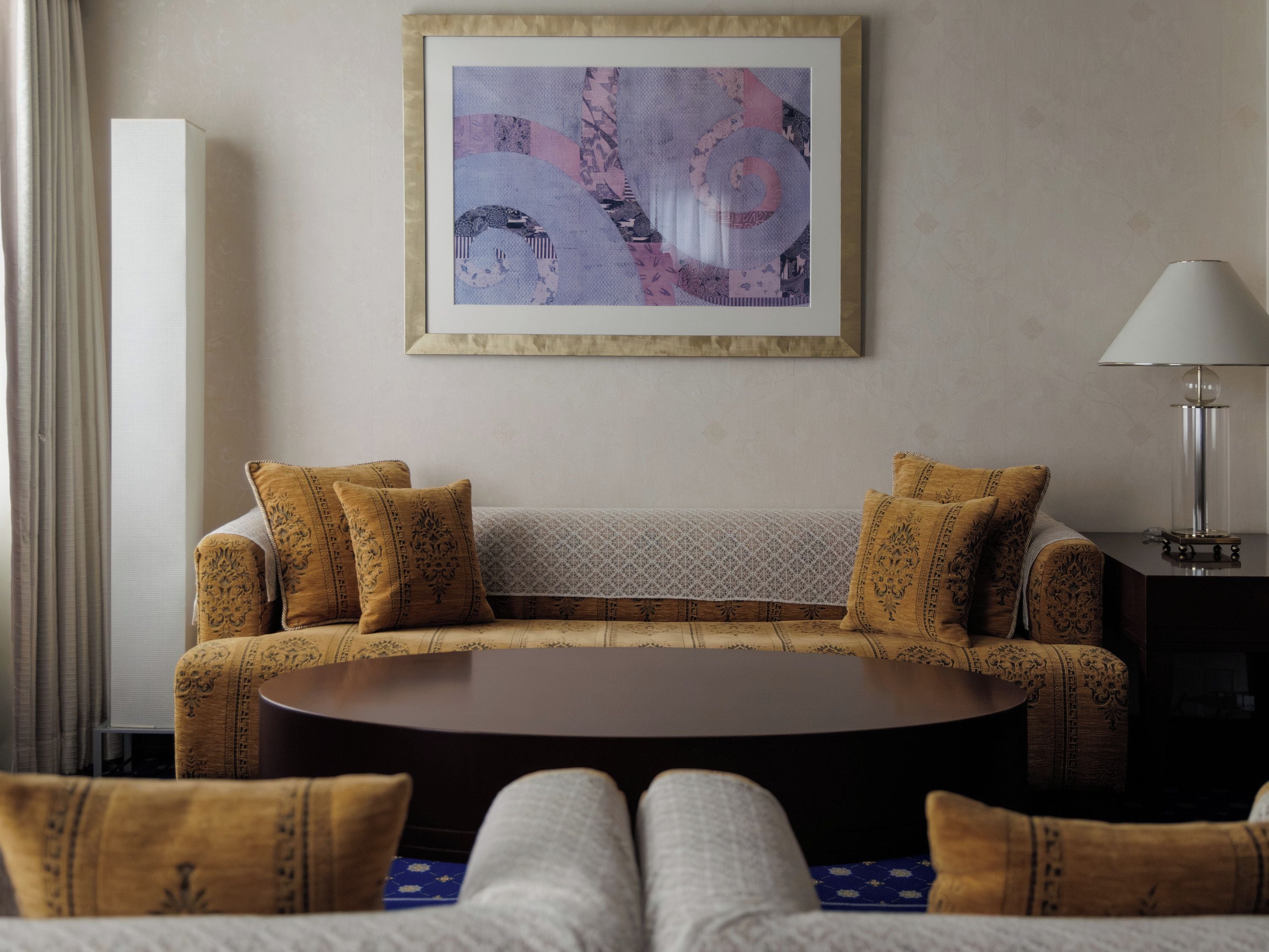 A room with a sofa, a table, a lamp, and a framed artwork on the wall.