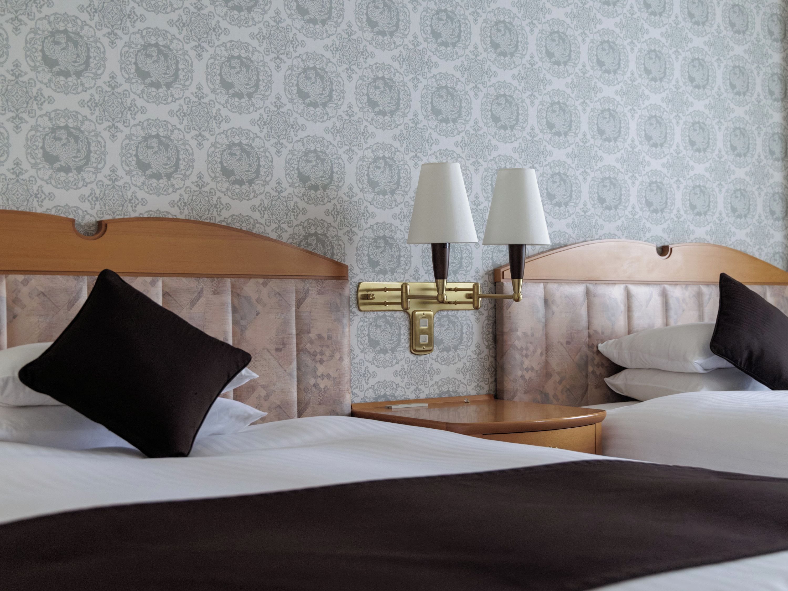 A hotel room with a bed, two bedside lamps, a nightstand, and a patterned wallpaper.