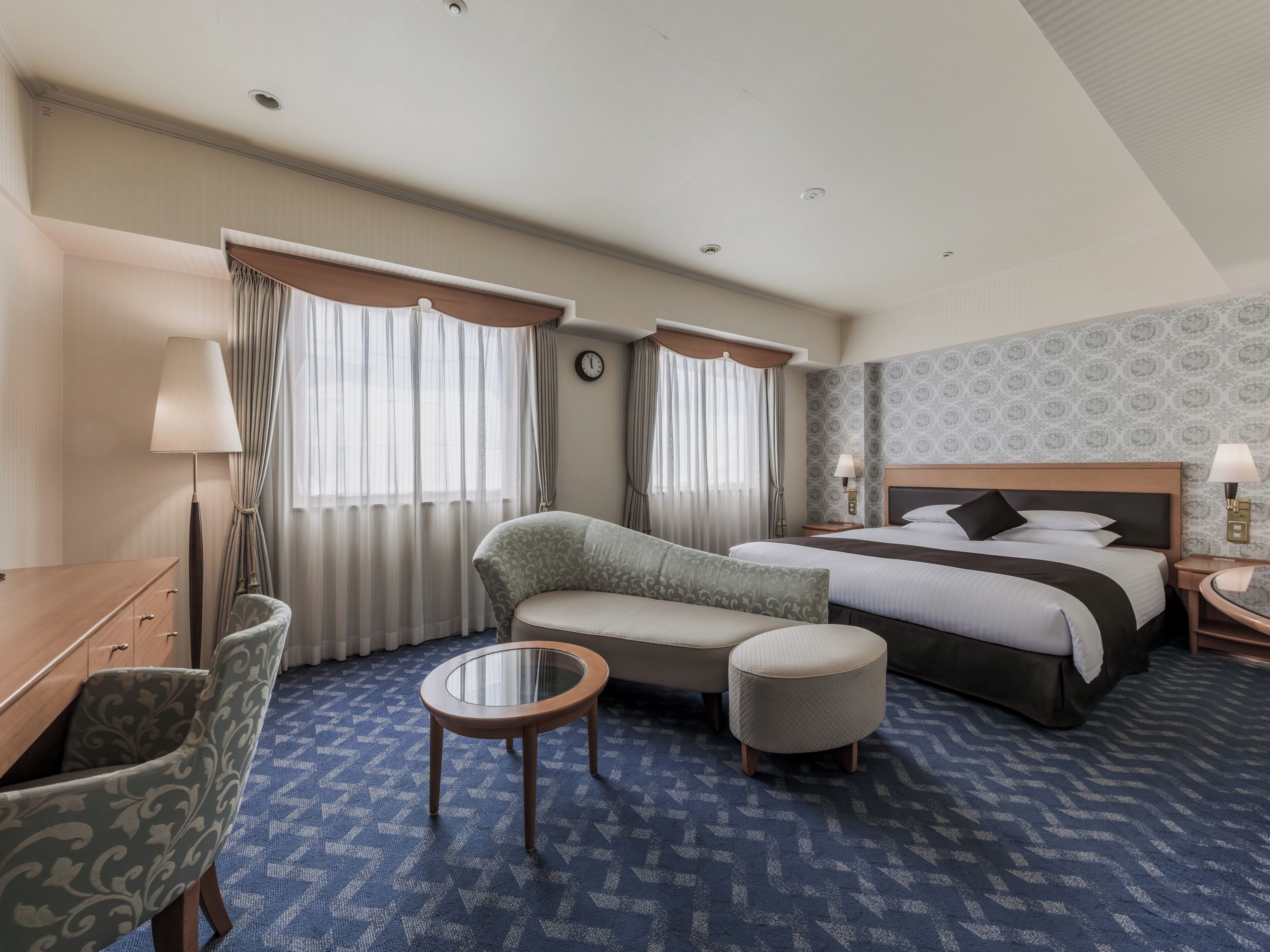 Una habitación de hotel con cama, sofá, sillón, una mesita y escritorio.