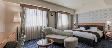 Una habitación de hotel con cama, sofá, sillón, una mesita y escritorio.