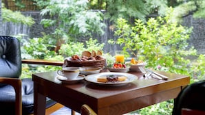 Una mesa de desayuno con diferentes platos, una taza y un vaso de jugo de naranja, con un exuberante jardín de fondo.