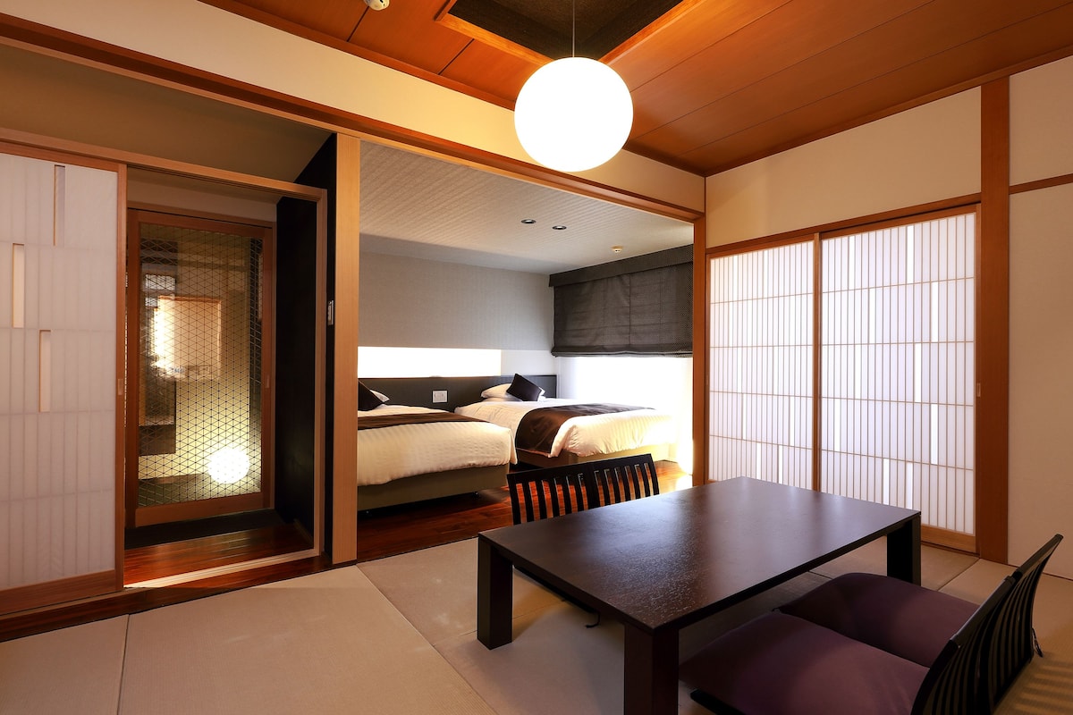 A traditional Japanese room with tatami flooring, a low table, and a bed with a futon.