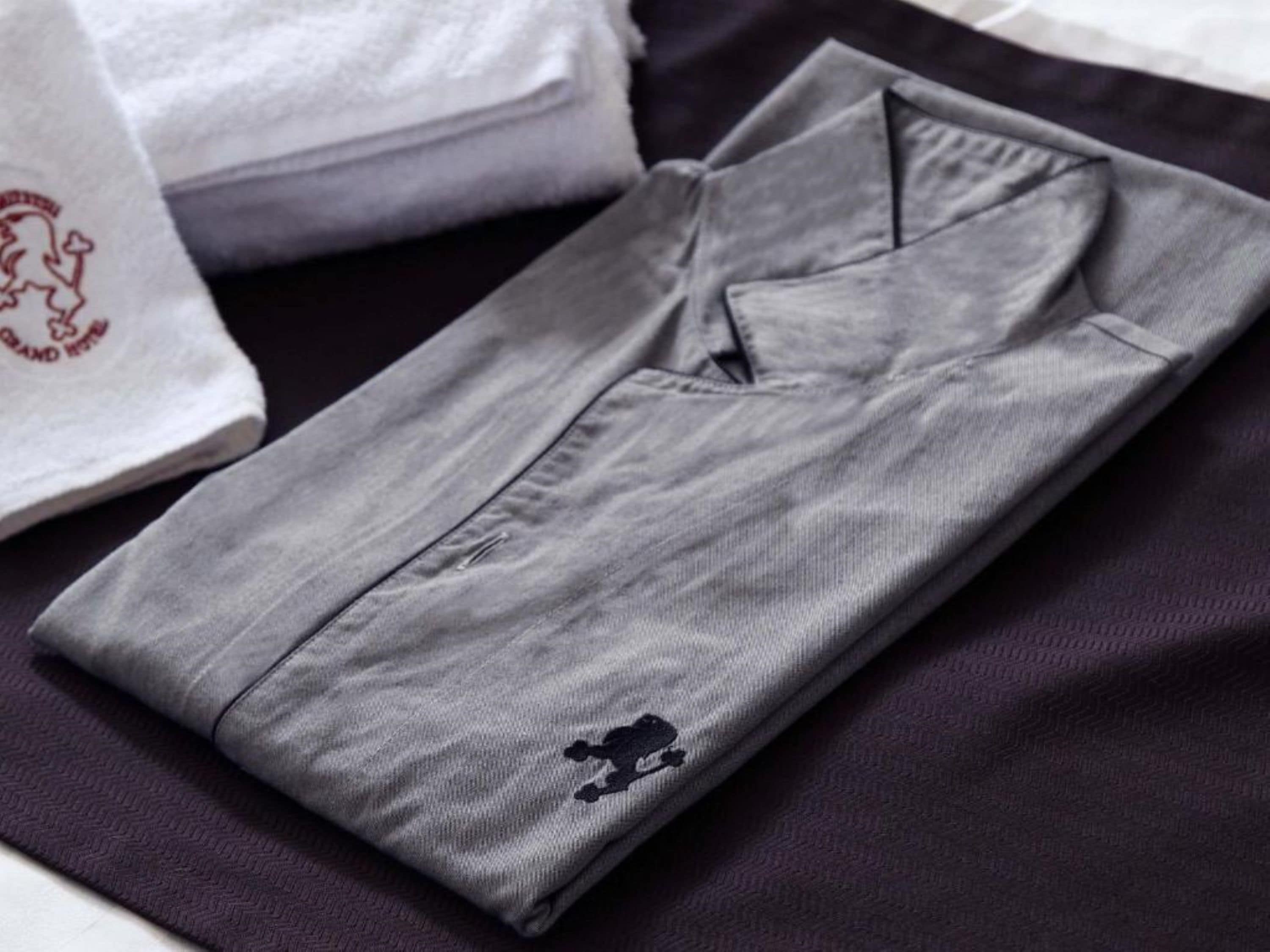 A neatly folded grey shirt with a small embroidered logo on the left chest area, placed on a dark fabric surface.