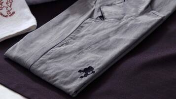 A neatly folded grey shirt with a small embroidered logo on the left chest area, placed on a dark fabric surface.