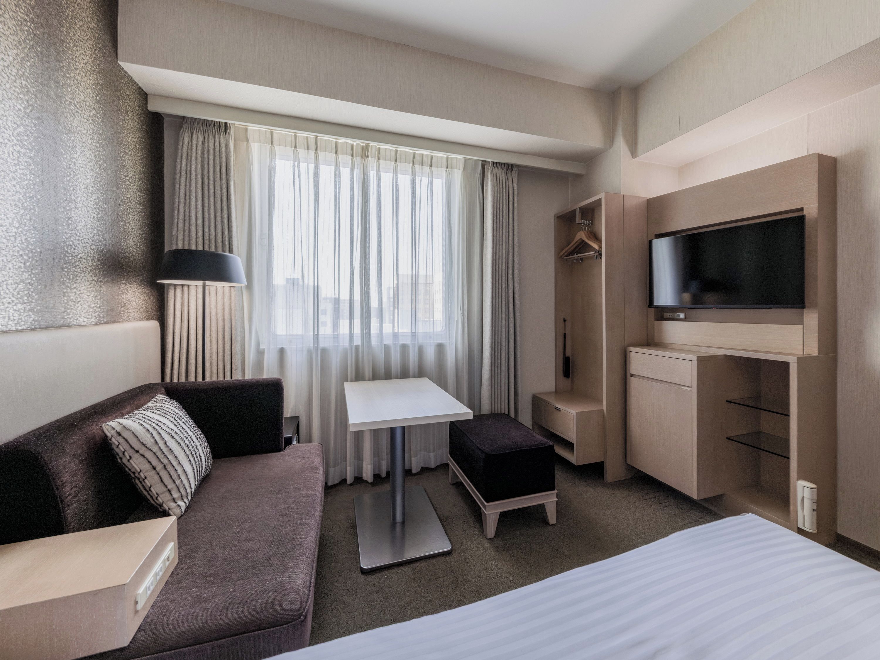 A hotel room with a bed, a sofa, a small table, a TV, and a wardrobe.
