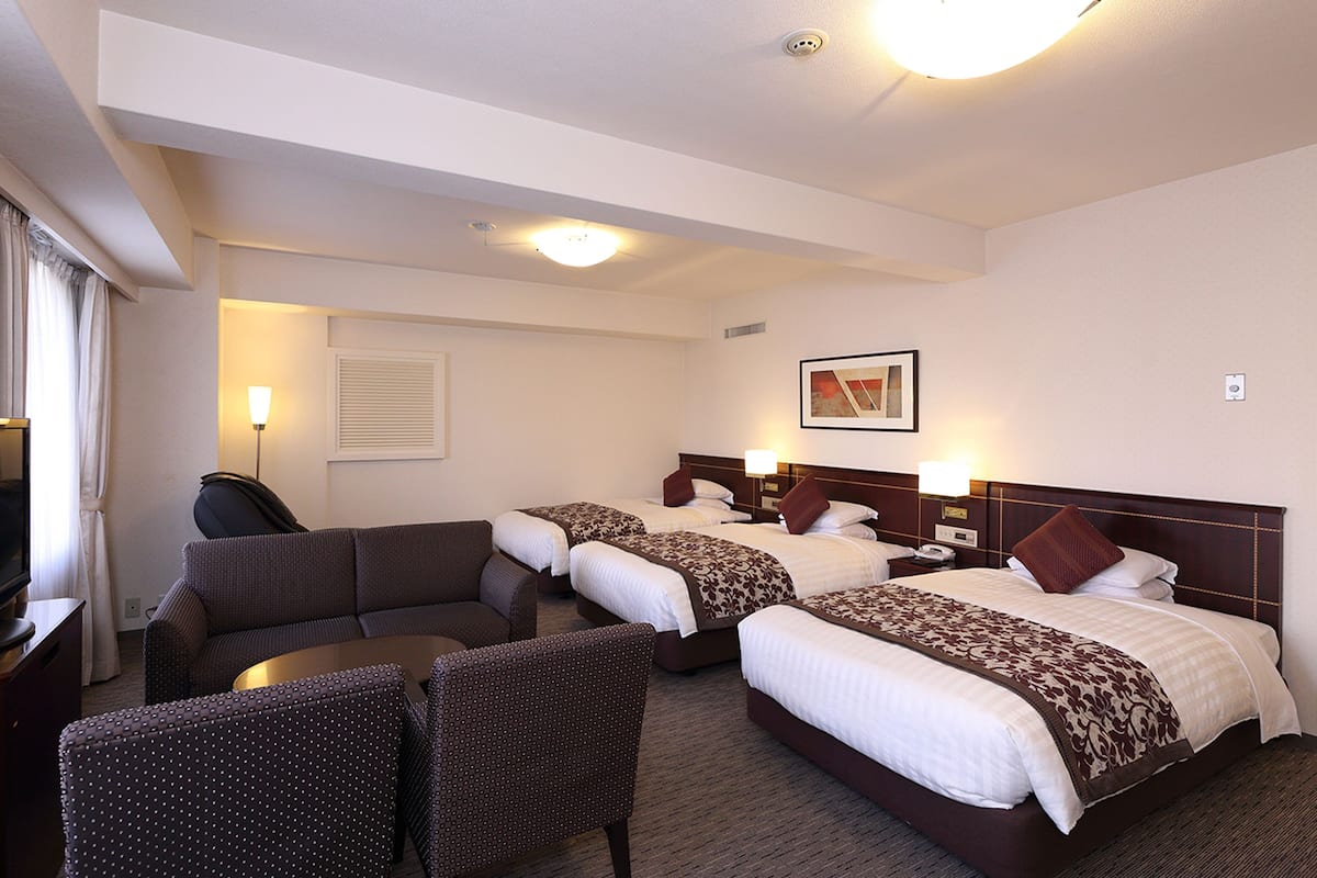 A hotel room with two beds, a sofa, and a TV.