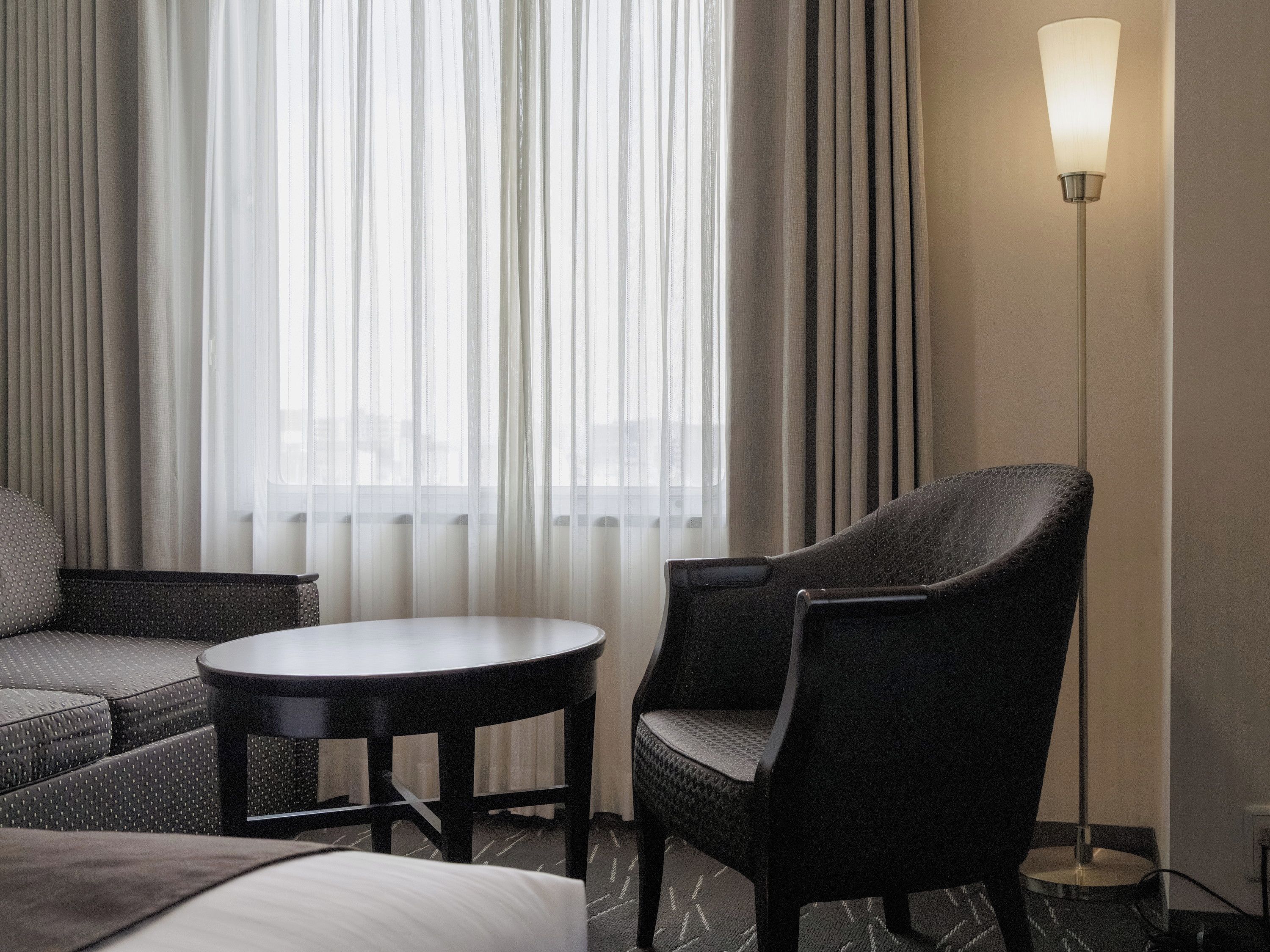 A hotel room with a bed, a round table, a chair, and a floor lamp.