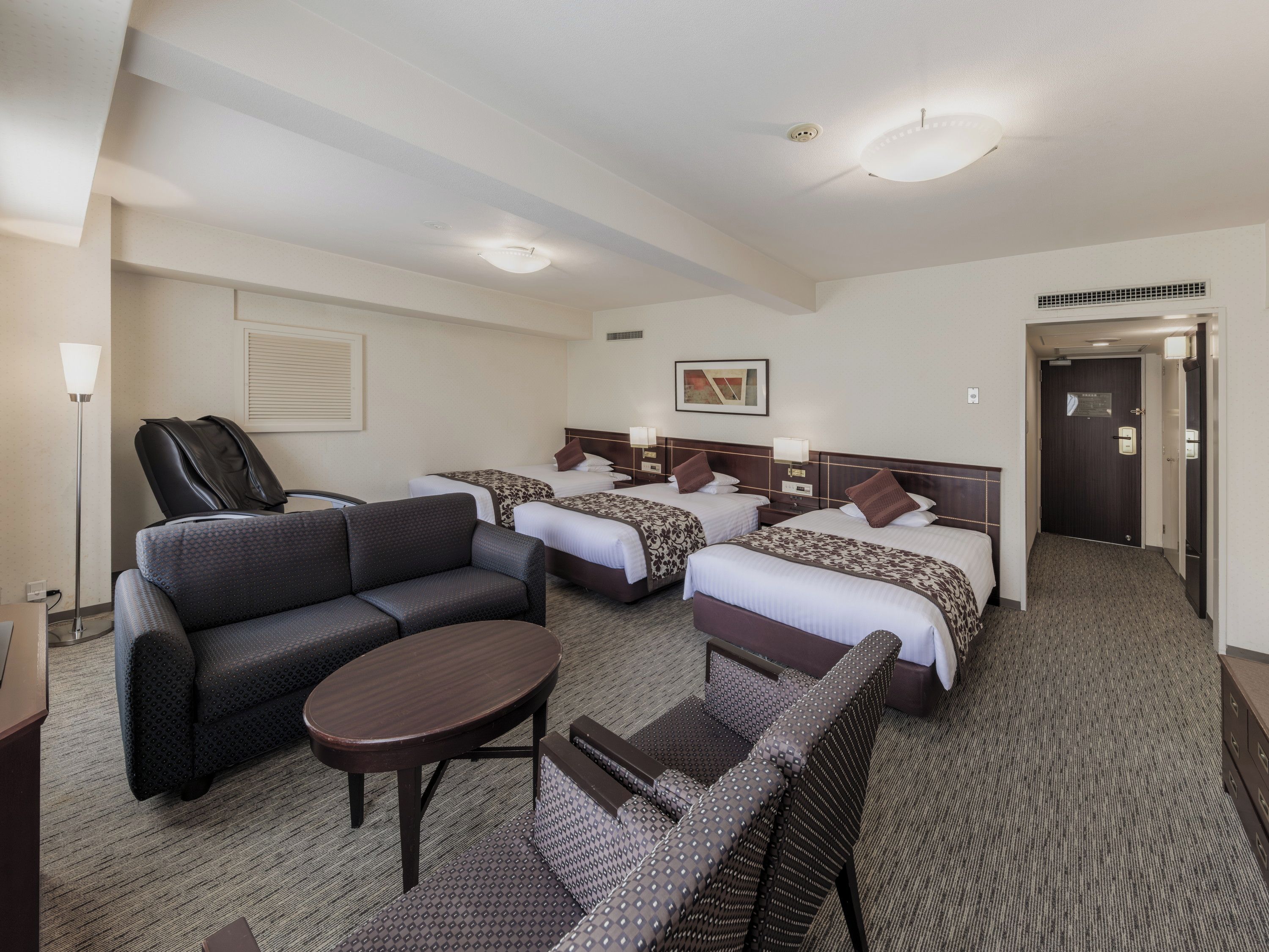 Ein Hotelzimmer mit einer Sitzecke, zwei Einzelbetten, einem Schreibtisch und einem Sessel.