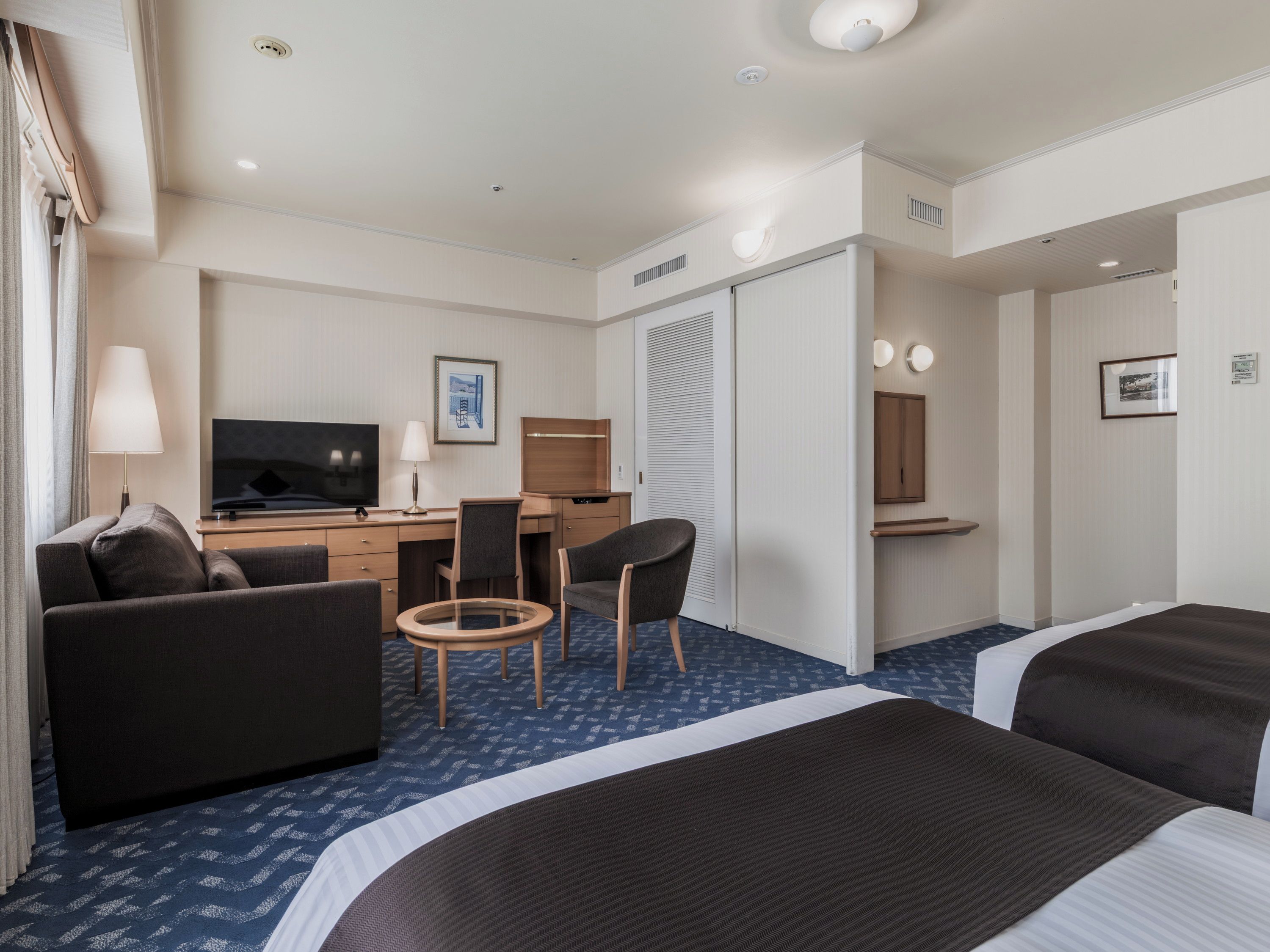 A hotel room with a bed, a sofa, a desk with a TV, a chair, and a small table.