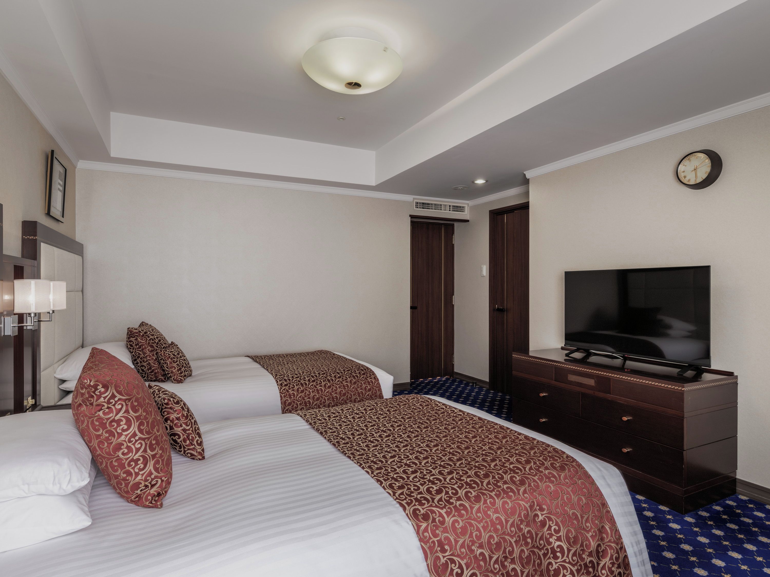 A hotel room with a bed, a television, a dresser, and a clock on the wall.