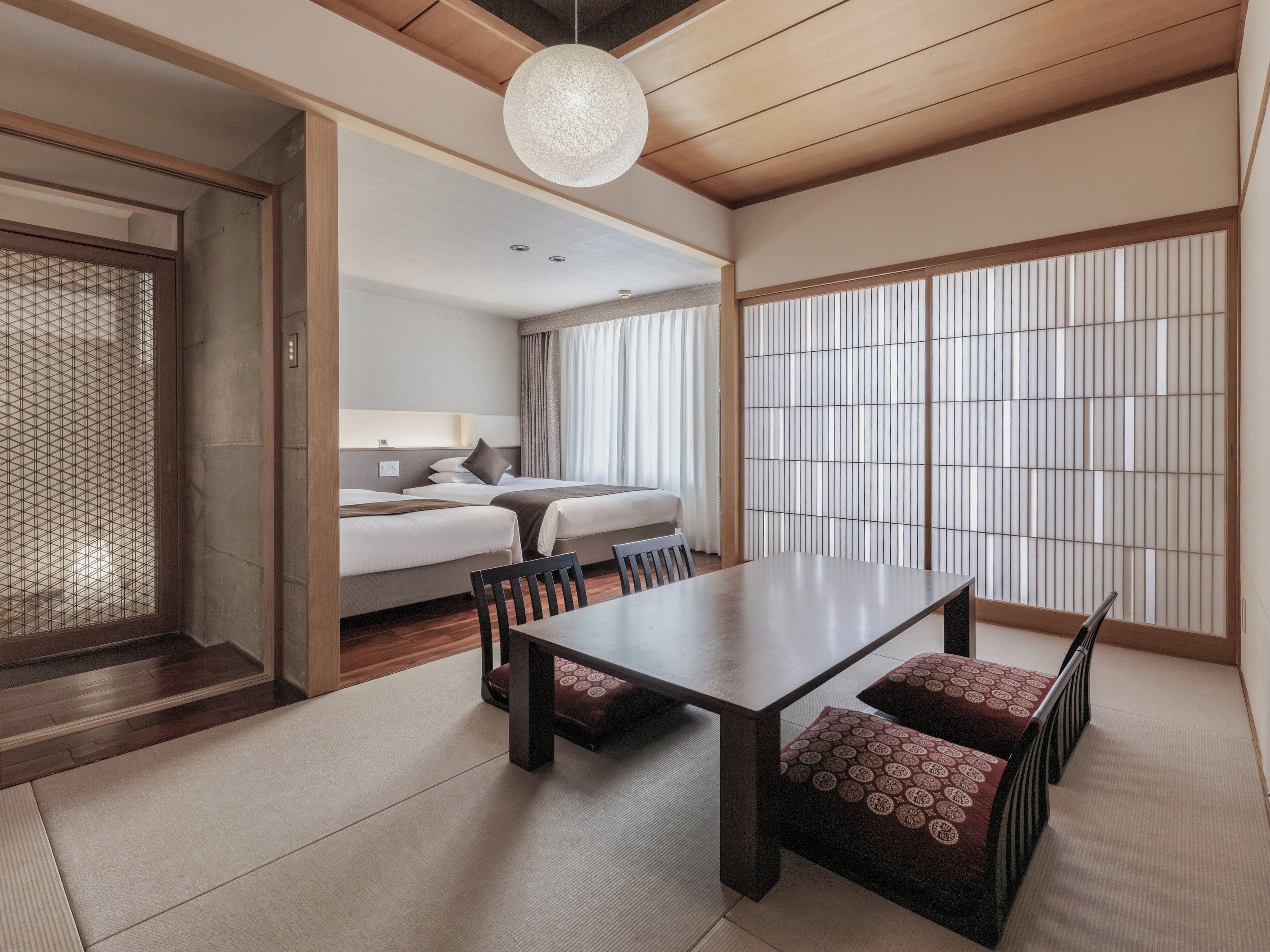 A traditional Japanese-style hotel room with tatami flooring, a low wooden ceiling, and a sliding shoji screen.