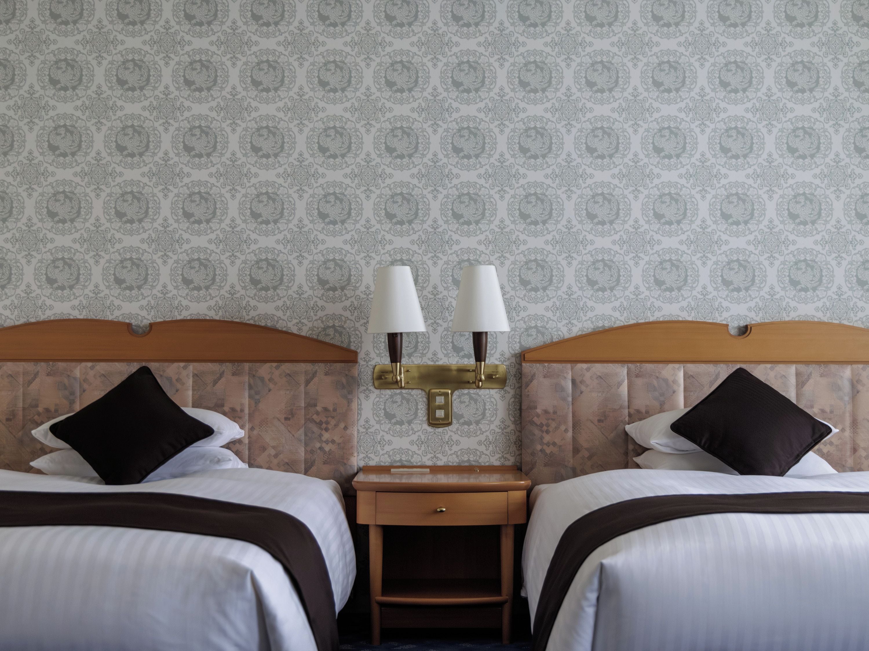 Une chambre d’hôtel avec deux lits, une table de chevet et une lampe fixée au mur.