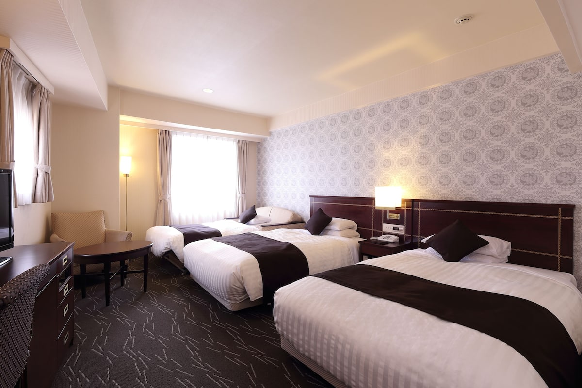 A hotel room with two beds, a desk, a chair, and a TV.