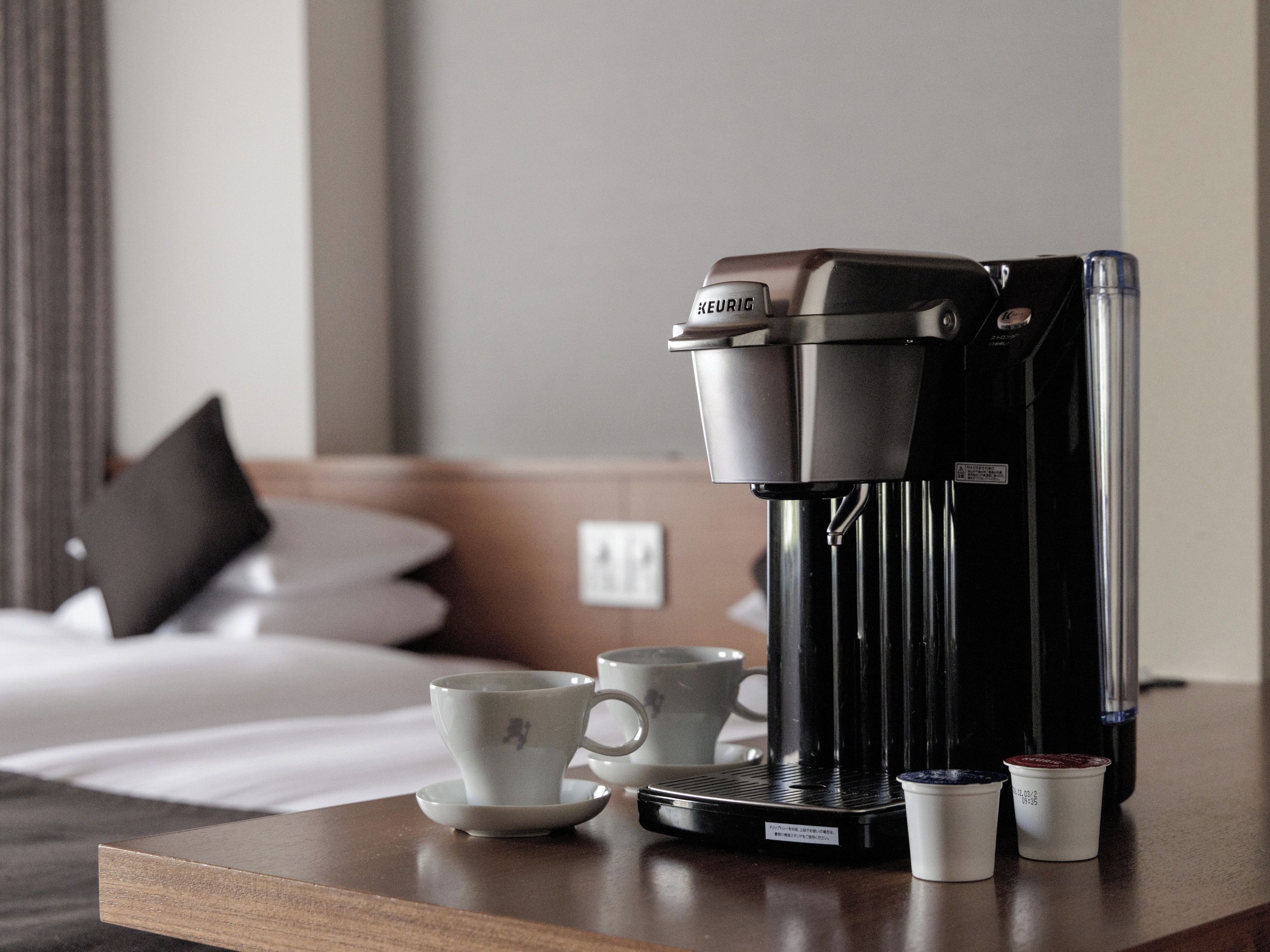 A coffee maker on a table with two cups and two small containers, likely for coffee grounds, in a hotel room setting.