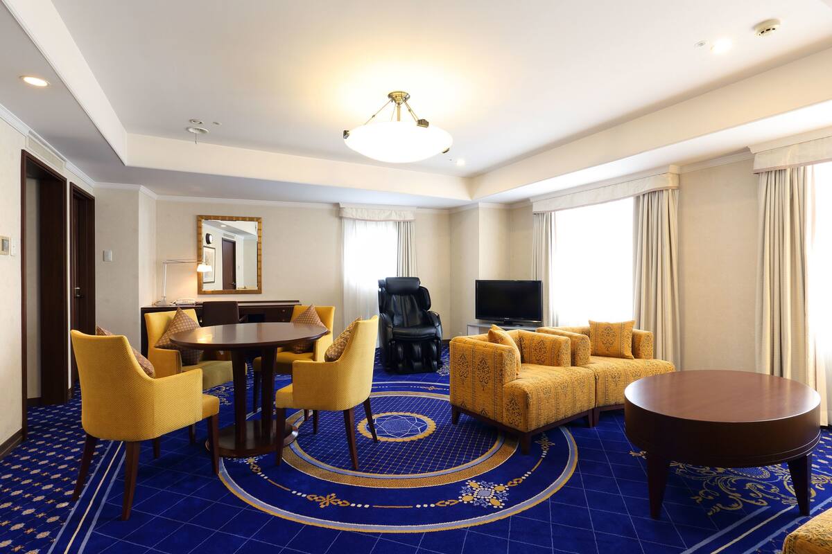 A hotel room with a dining area, a sofa set, a TV, and a massage chair.