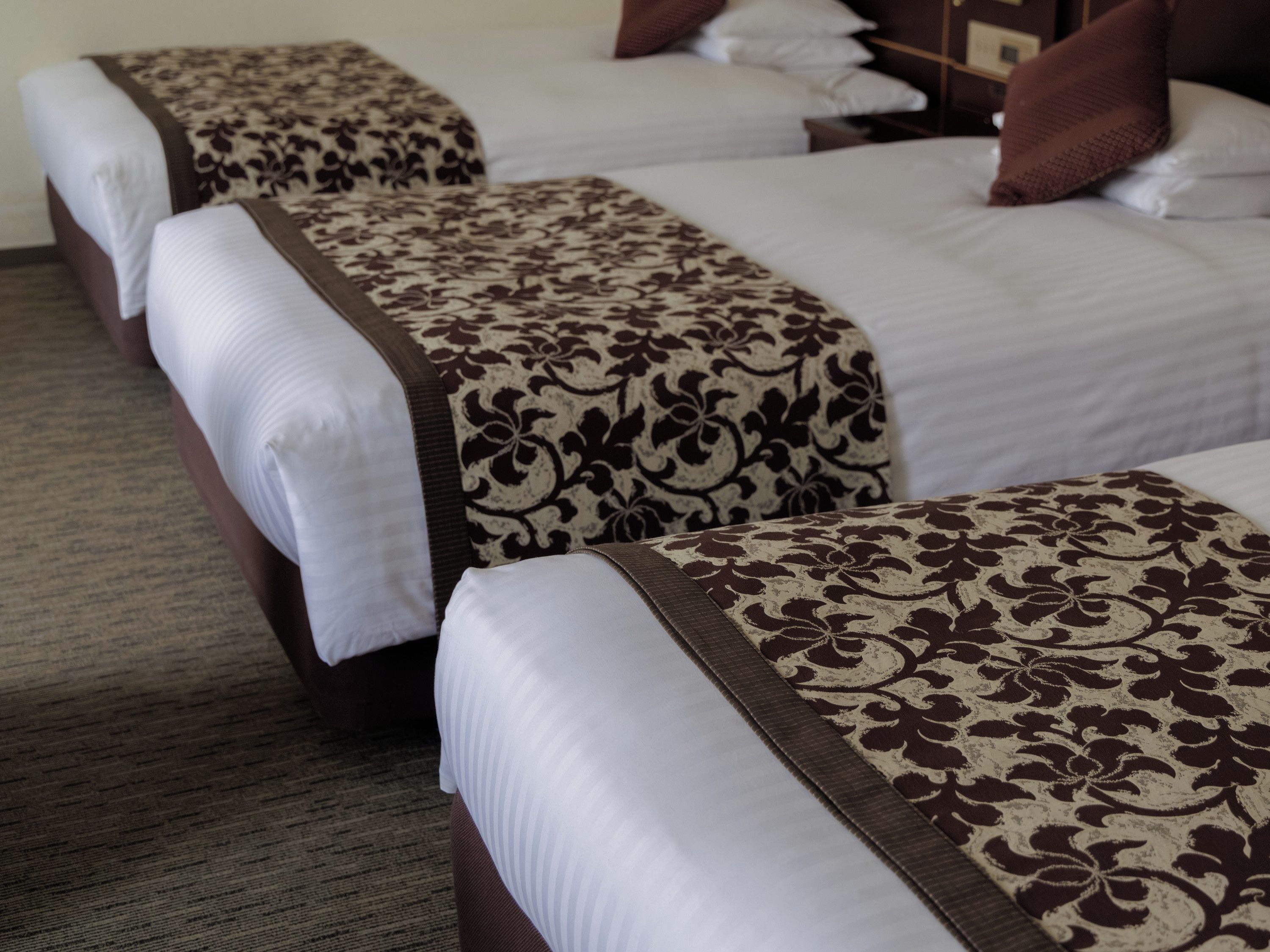 Habitación de hotel con tres camas dispuestas en fila, cada una con un edredón estampado y almohadas blancas.