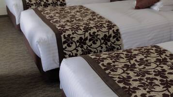 Habitación de hotel con tres camas dispuestas en fila, cada una con un edredón estampado y almohadas blancas.