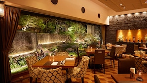 Restaurante con vistas a un jardín y una cascada, con sillas y mesas de diseño.