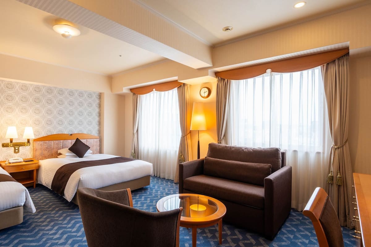 A hotel room with two beds, a sofa, a small table, and a lamp.